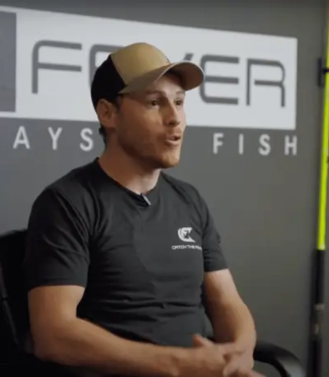 Catch The Fever CEO Kaleb Page seated in headquarters, wearing a branded charcoal tee and tan cap, discussing company strategy.